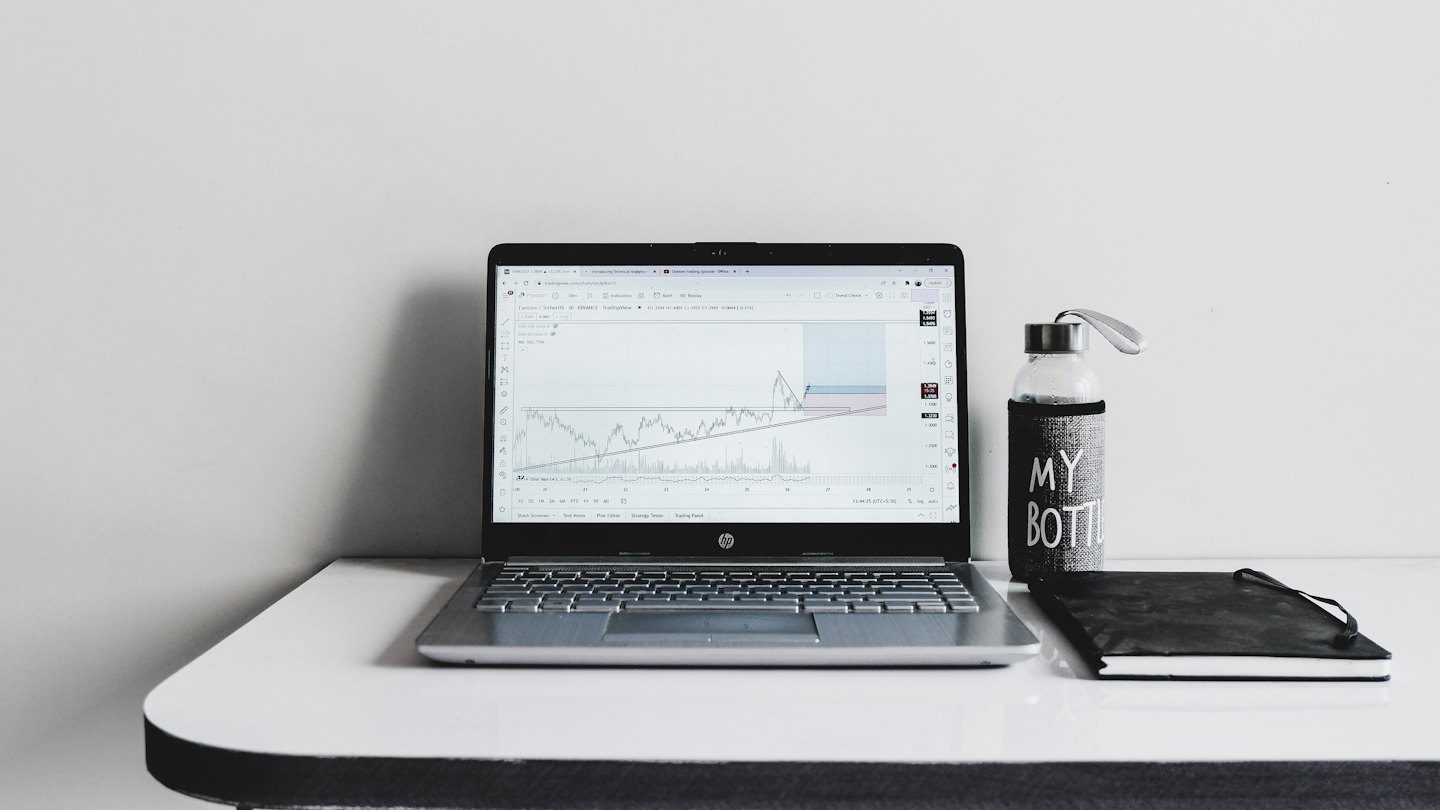 Laptop mit Finanzdiagrammen neben Notizbuch und Wasserflasche.